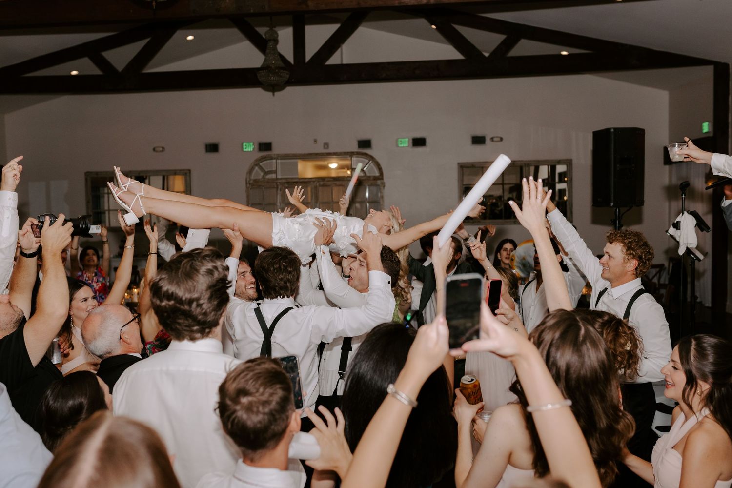 Energetic wedding reception crowd lifts bride above their heads on dance floor.