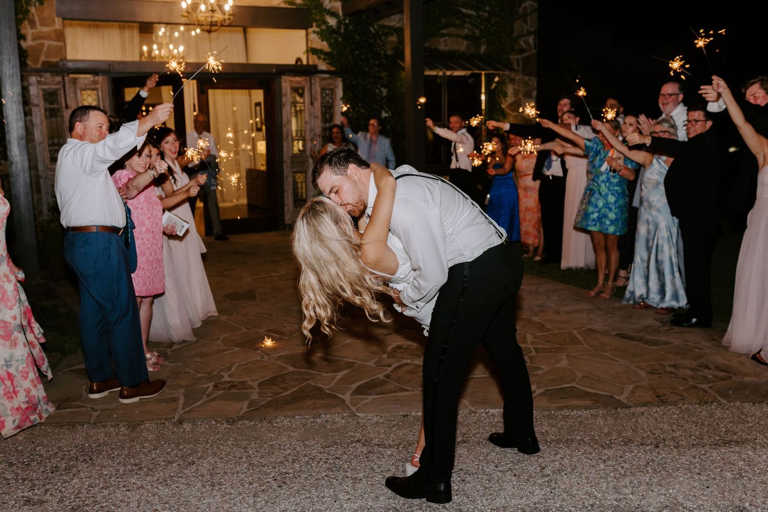 Wedding guest performs entertaining dance moves on outdoor patio during evening reception.
