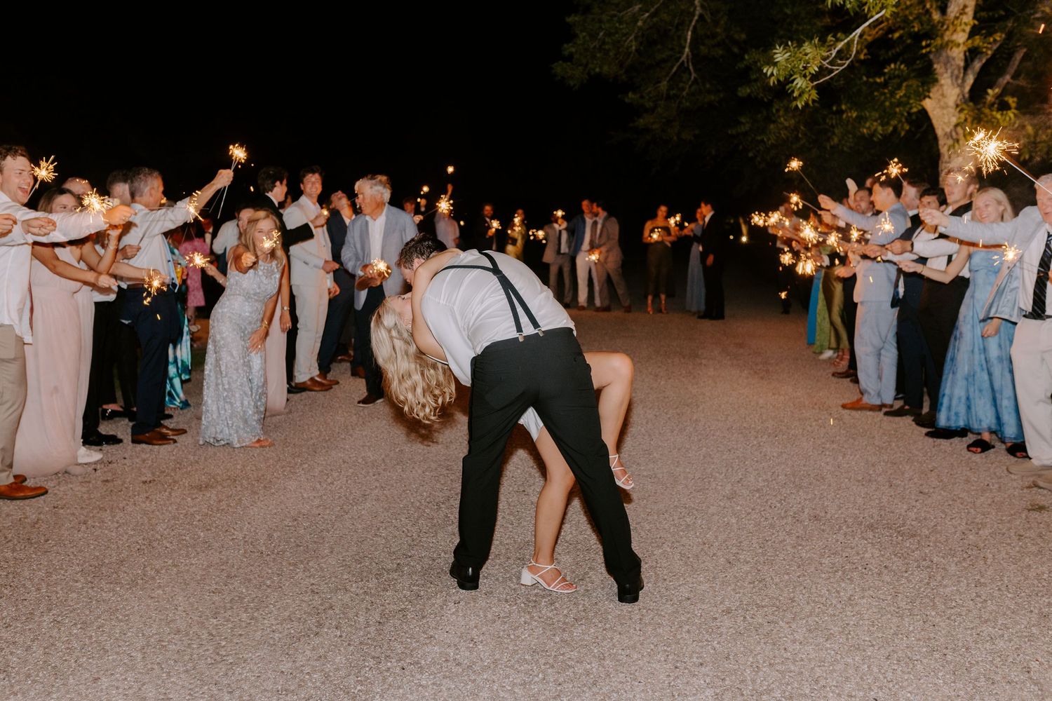 Couple bows during sparkler exit sendoff with guests forming illuminated pathway.