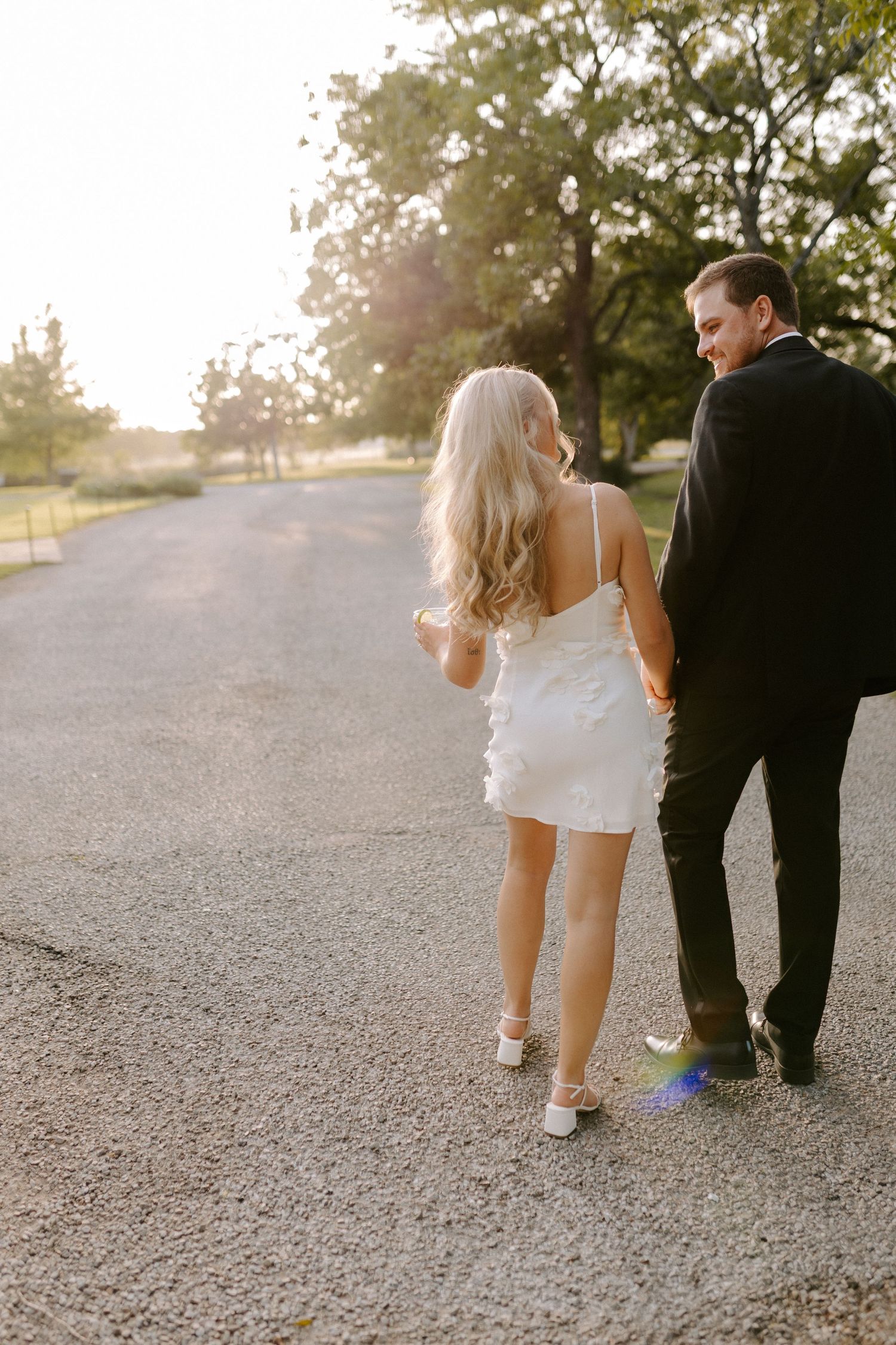 A couple walks down a sunlit path together during their wedding photoshoot.