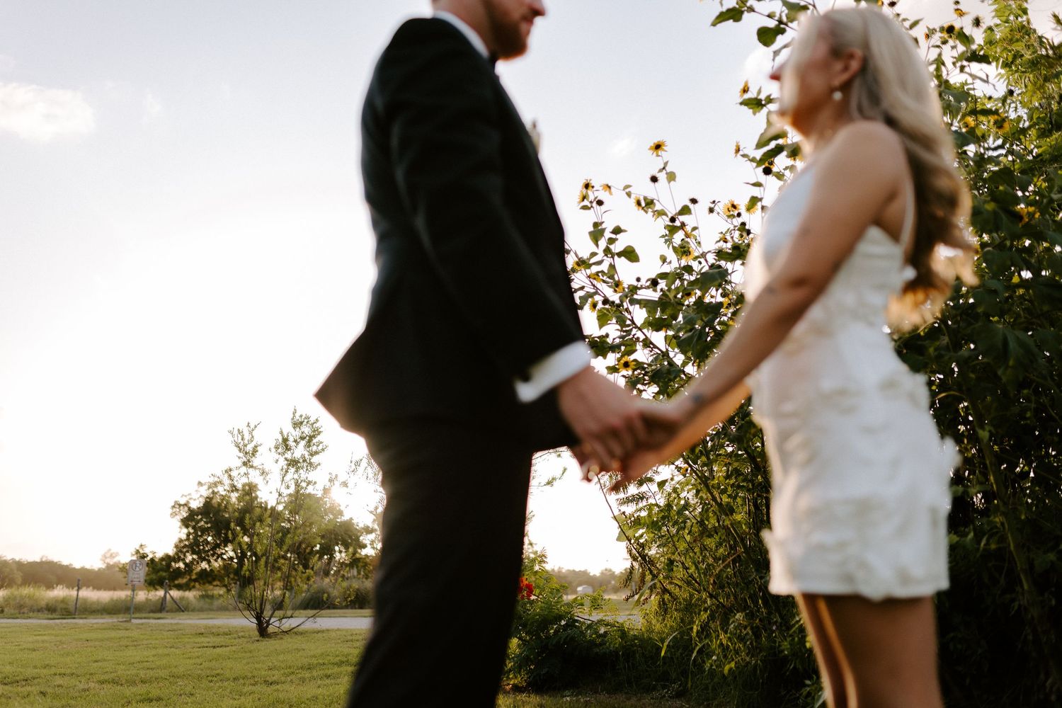 Bride and groom hold hands during golden hour in a romantic outdoor setting.