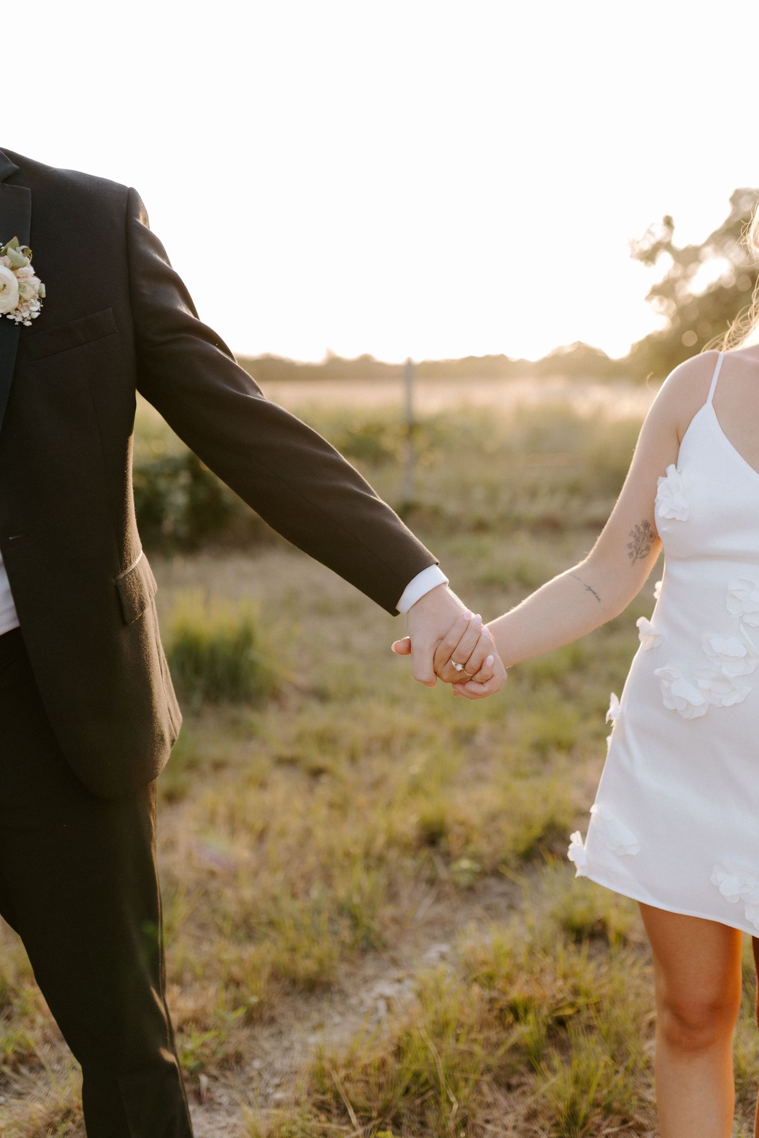 Romantic sunset photo of newlyweds holding hands in a rustic outdoor field setting.