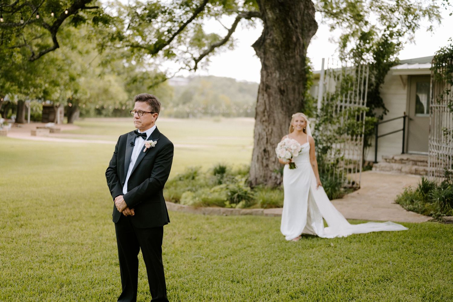 Elegant outdoor first look moment between couple under large oak tree.