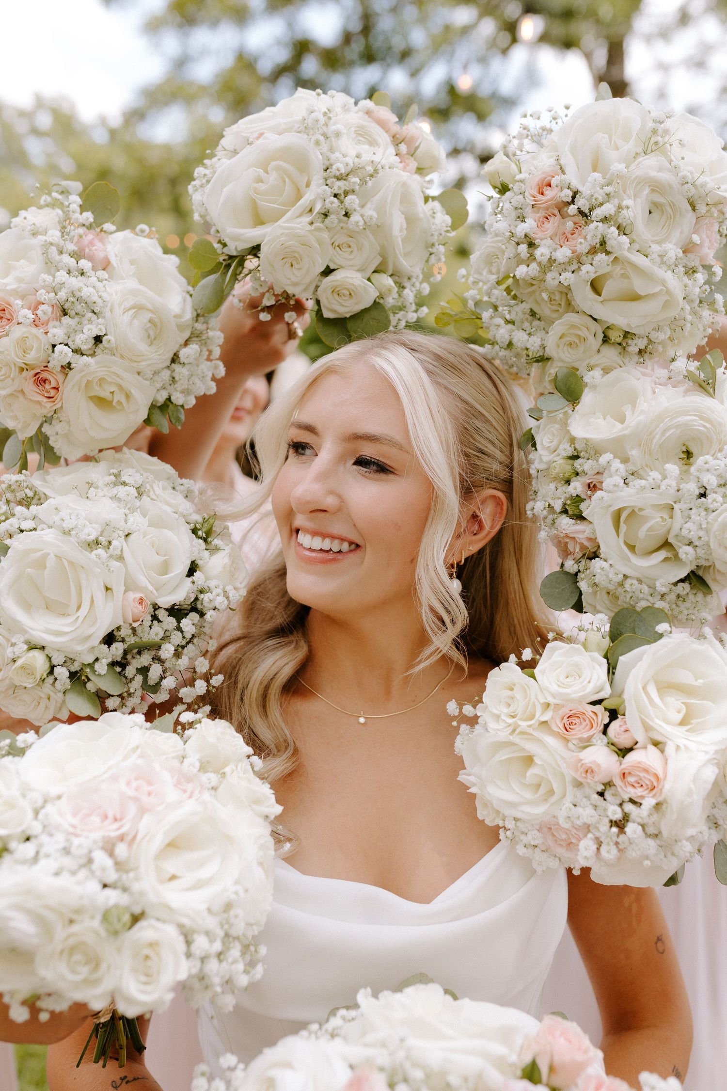 Beautiful wedding bouquets with white roses and baby's breath flowers held up in natural outdoor lighting.
