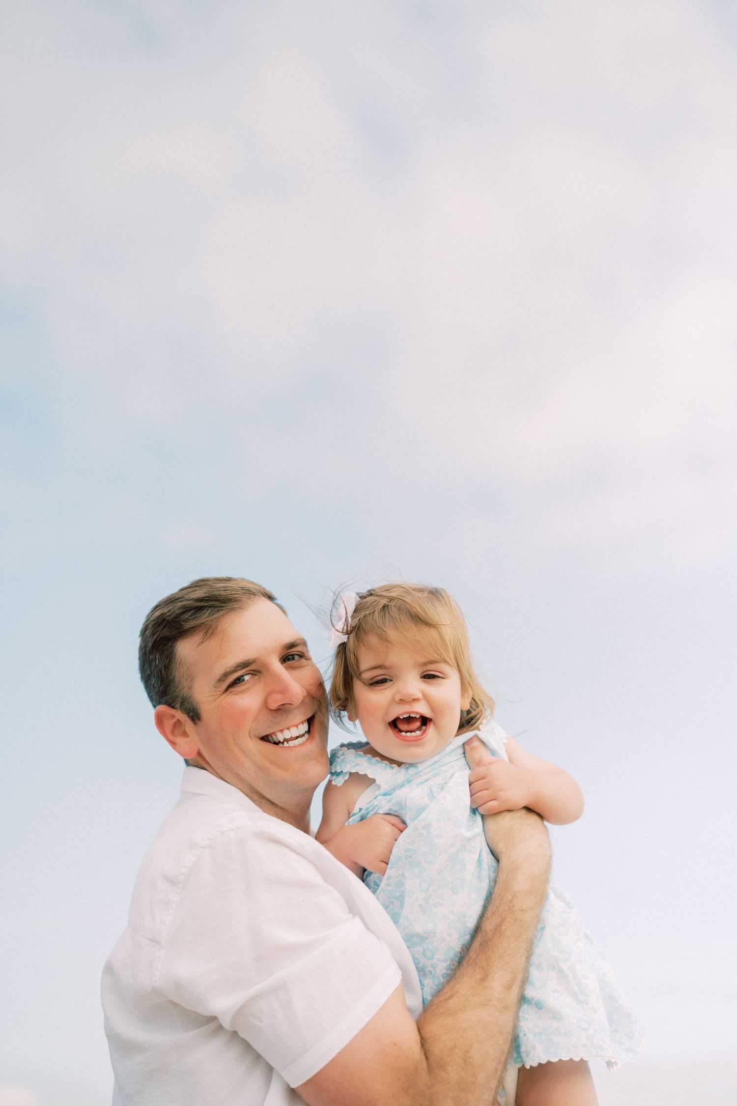 A parent and child share a joyful moment together against a soft blue sky background.