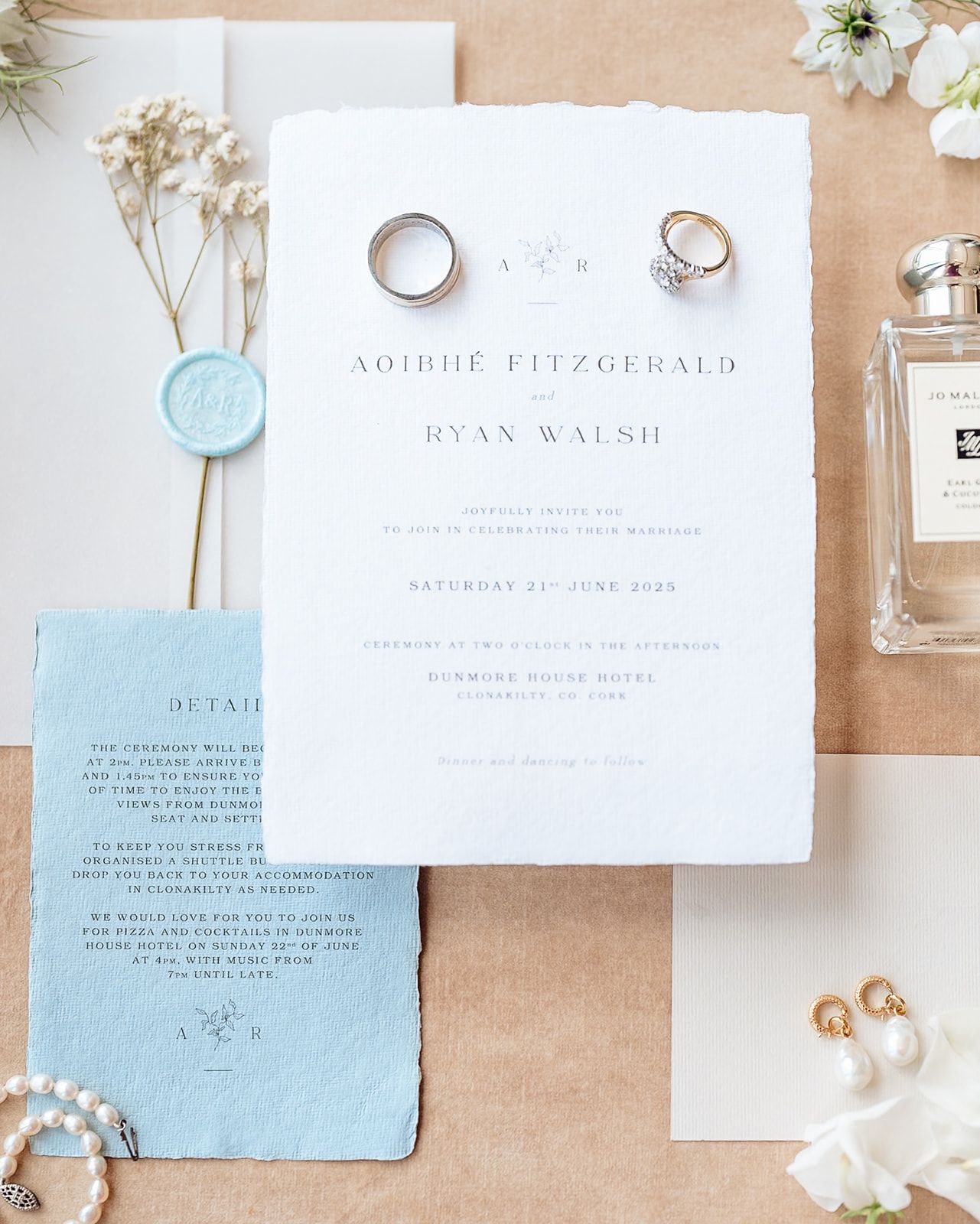 Elegant wedding invitation suite with deckled edge blue paper and white floral accents arranged on a neutral background.