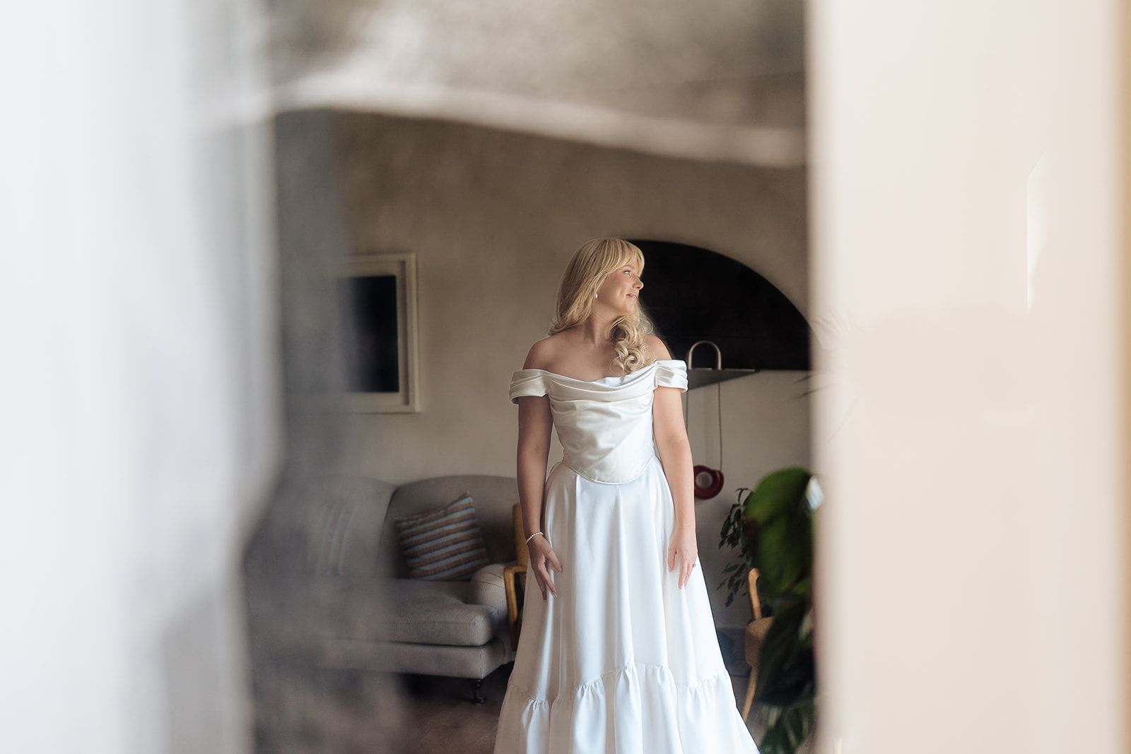 Elegant off-shoulder white wedding dress captured in a dreamy interior setting with soft natural lighting.