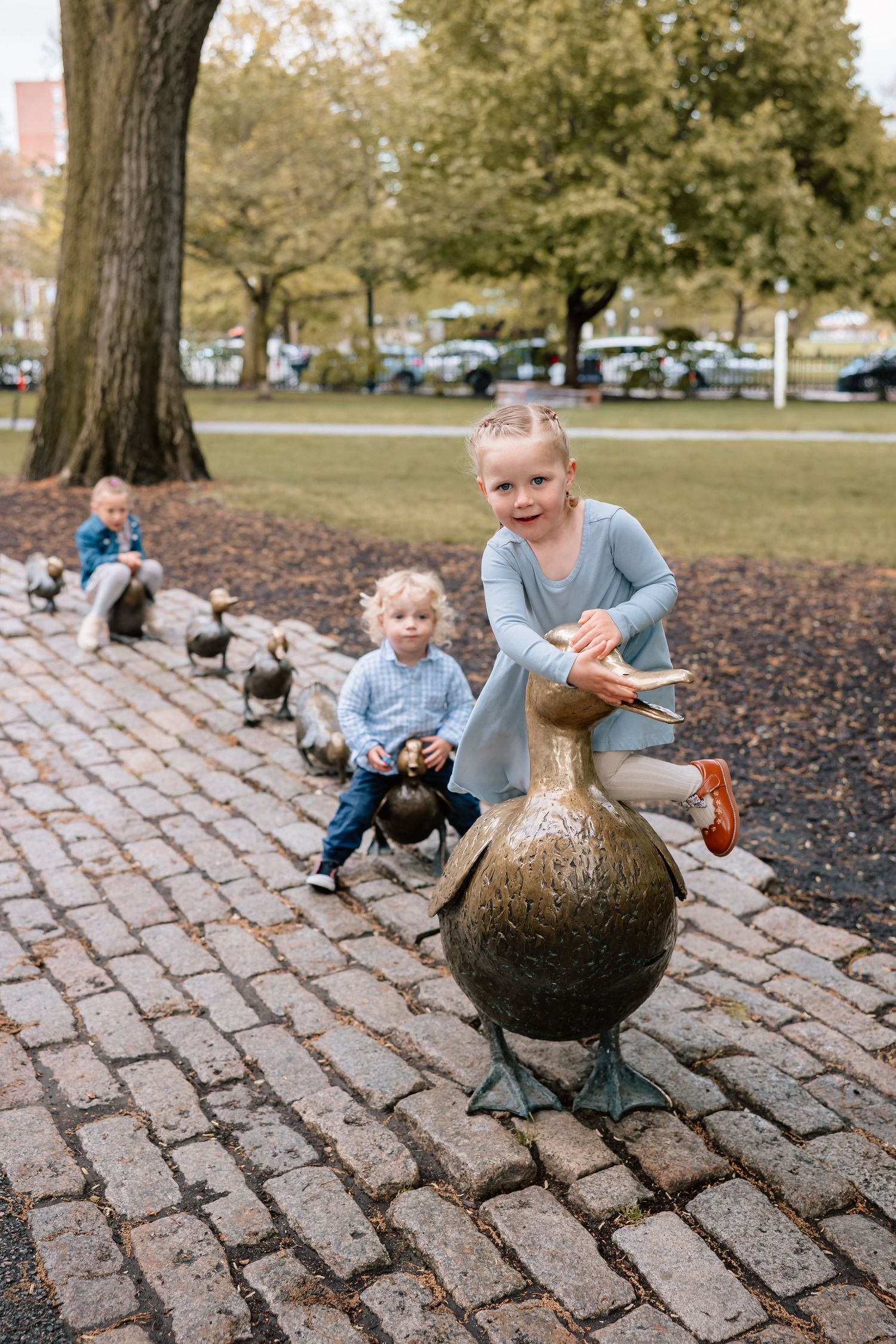 A person in a blue sweater playing with a bouncy ball on a cobblestone path in a park setting.