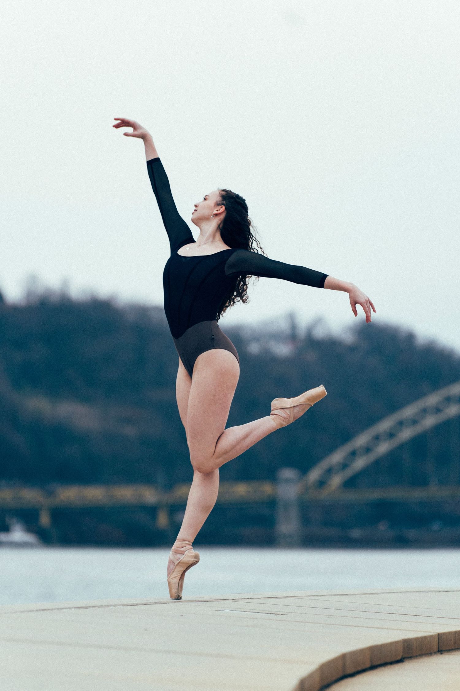 Fine art ballet photography featuring a ballerina posing with downtown Pittsburgh bridge behind her pittsburgh dance photoshoot