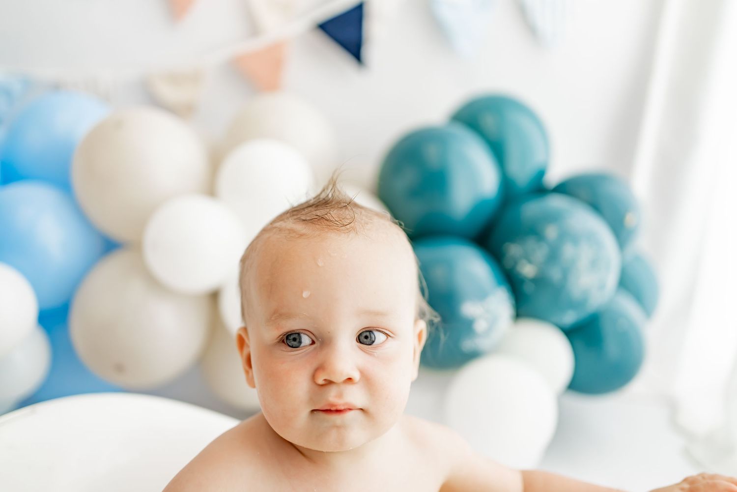Cake smash photo session setup with white and turquoise balloons and decorations for milestone celebration.