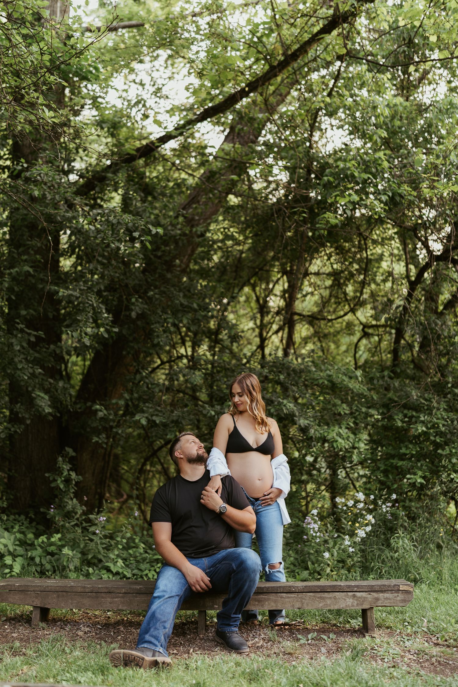maternity photos in pittsburgh pennsylvania by ash coniglio photography, man sitting on bench while woman stands, he looks up at her smiling