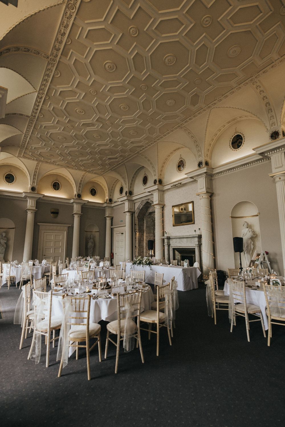 Elegant ballroom with ornate ceiling featuring geometric patterns and round tables set for formal dining at white-clothed tables.