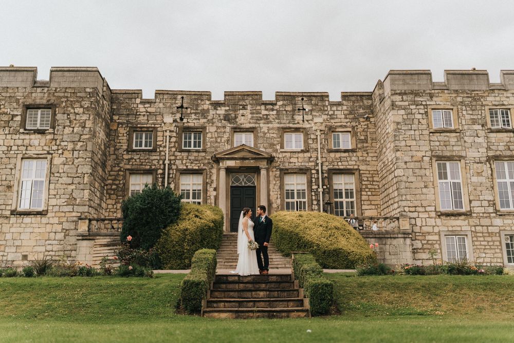 Stone castle exterior walls create a rustic backdrop for a wedding day photograph in natural light.