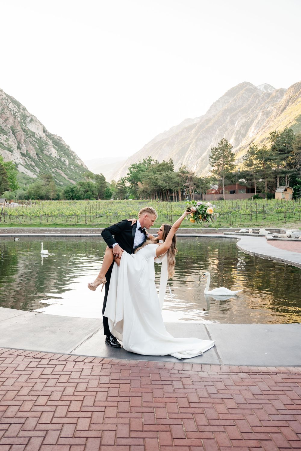 A romantic dip pose against a mountain backdrop at a lakeside wedding venue with stunning natural scenery.