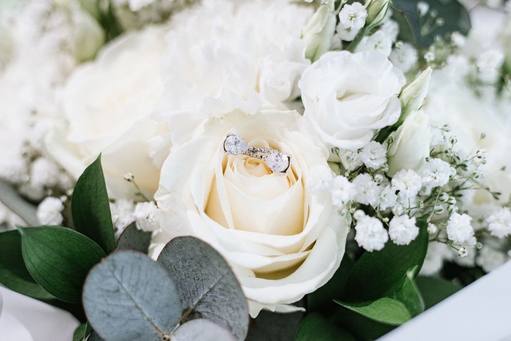 Two gold wedding rings nestled inside a cream white rose bloom with eucalyptus leaves and baby's breath florals.