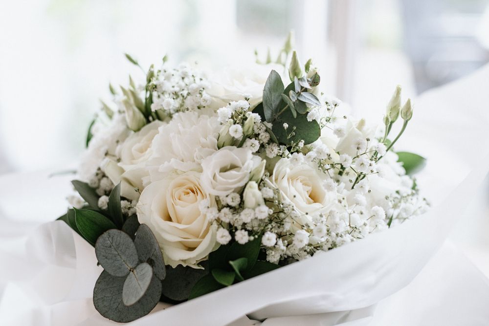A delicate white bouquet with cream roses, baby's breath flowers and eucalyptus leaves wrapped in soft white paper.