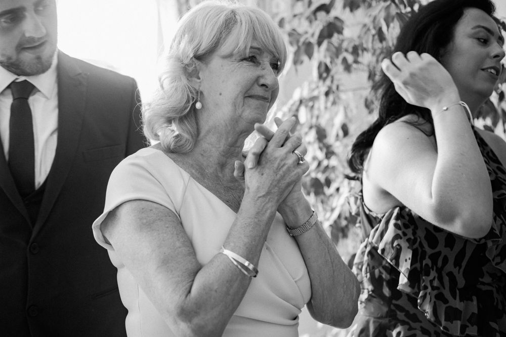 Black and white candid photo of guests at a formal event, with a woman in a sleeveless dress applauding.