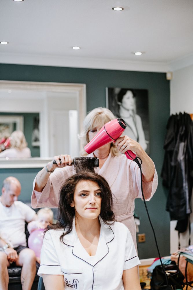 Several pairs of hands holding hair dryers while styling hair in a bright modern salon interior.