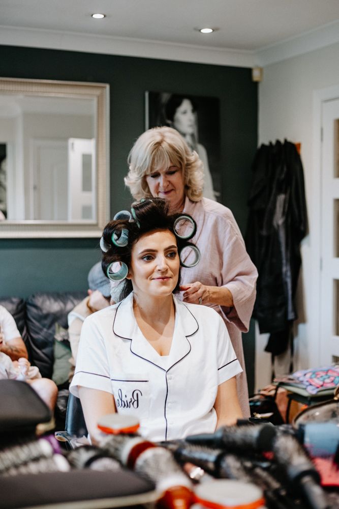 Two people in a dressing room with makeup and styling tools scattered on the counter while preparing for an event.