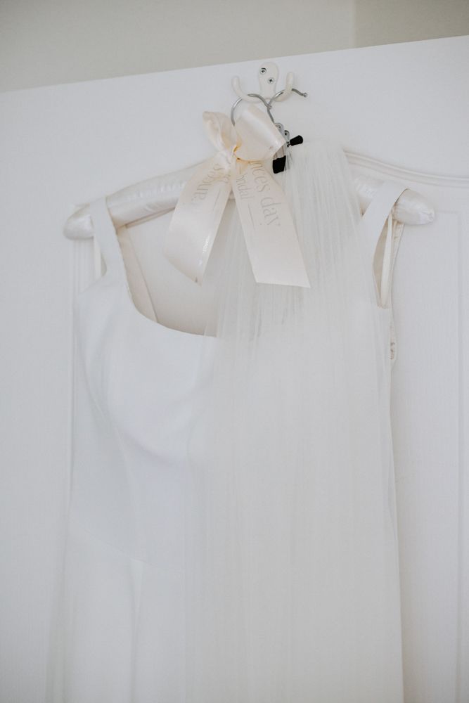 Multiple white bridal dresses hung on hangers against a light colored wall.