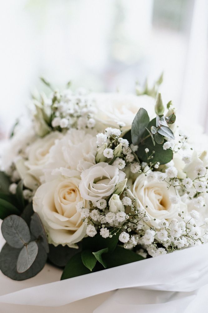Elegant white rose bouquet with soft pink accents and baby's breath flowers wrapped in white silk ribbon.