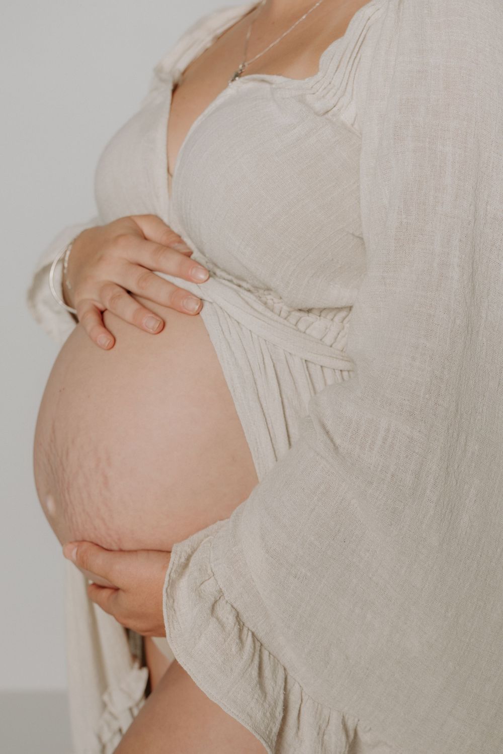 Close-up side view of pregnant belly draped in soft white linen fabric during maternity photoshoot.