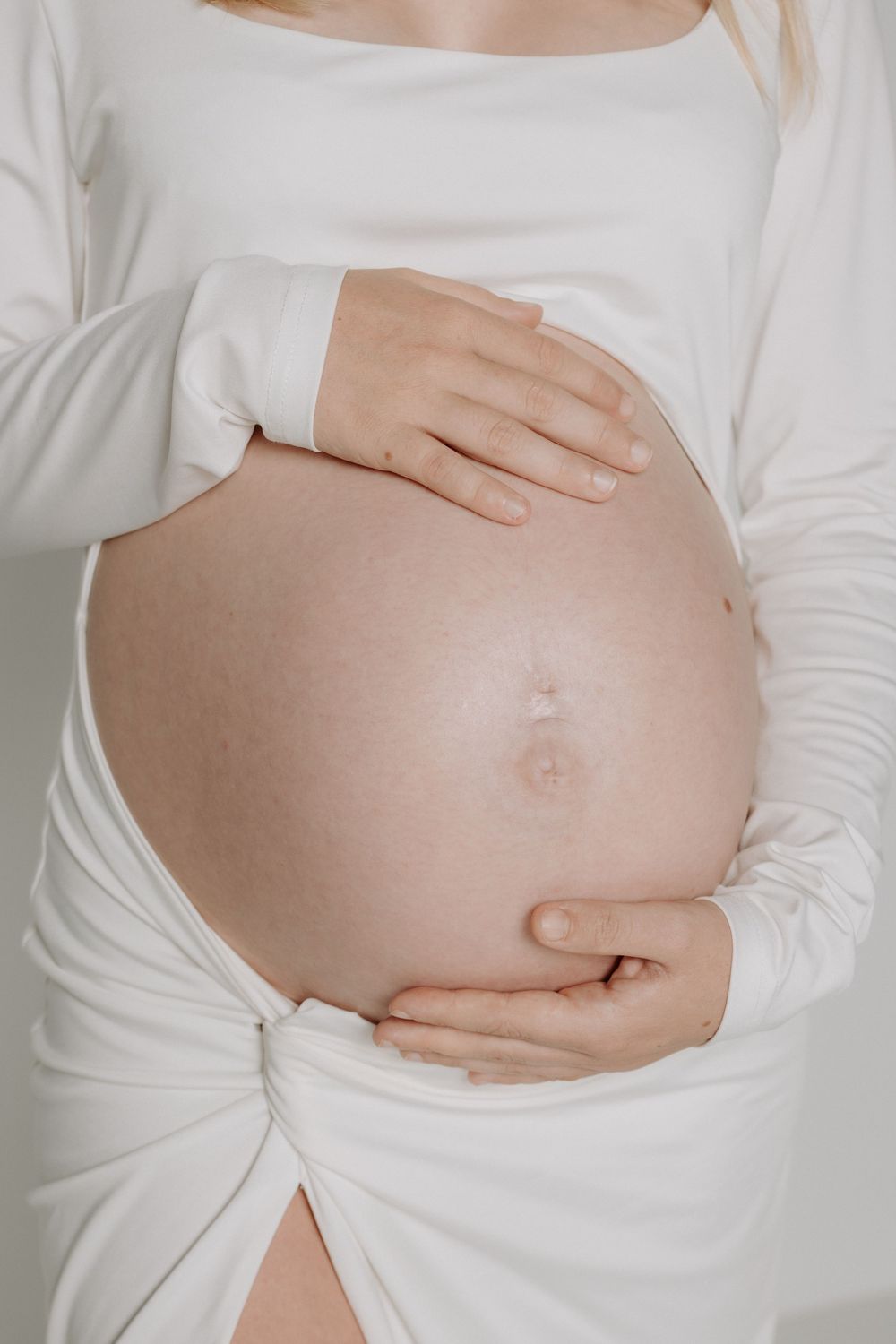 Close-up of a pregnant belly being cradled by hands against white fabric.