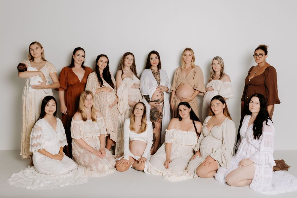 A group in neutral-toned outfits poses together on a light backdrop for an elegant studio portrait.