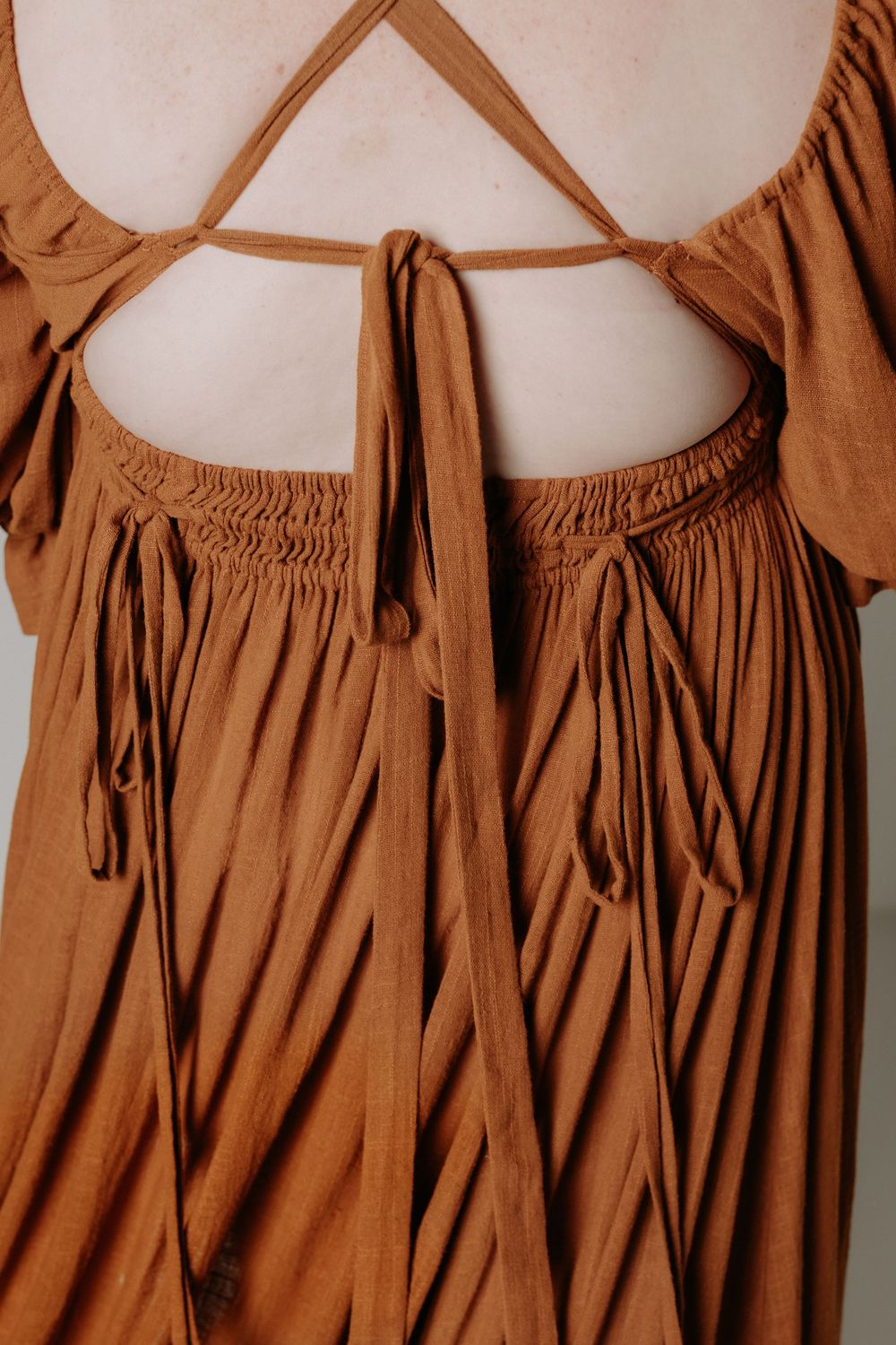 Close-up detail of a rust-colored gathered dress with tie straps and smocking texture.