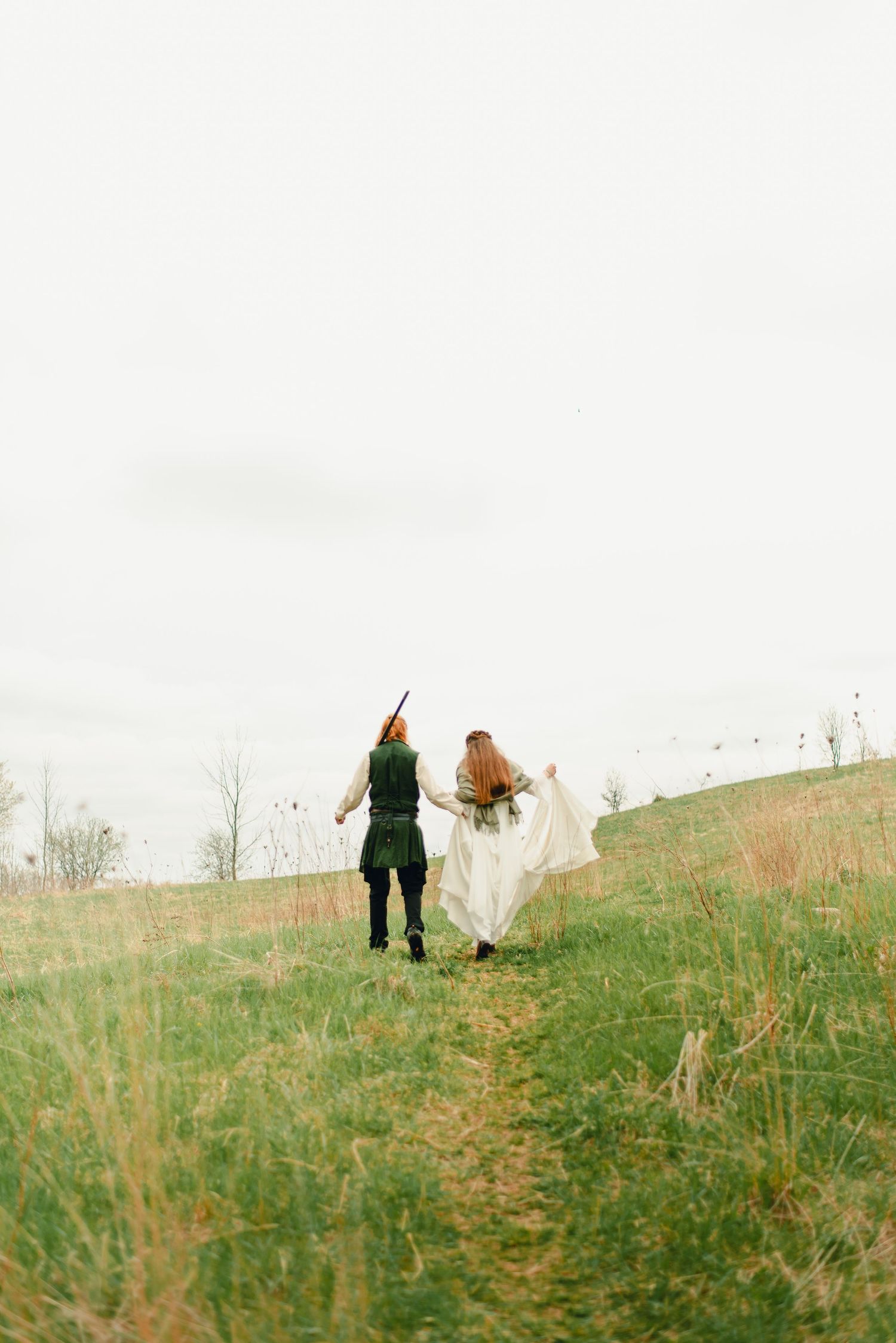 Bride and groom running through the fields together in a cloudy forest clearing.