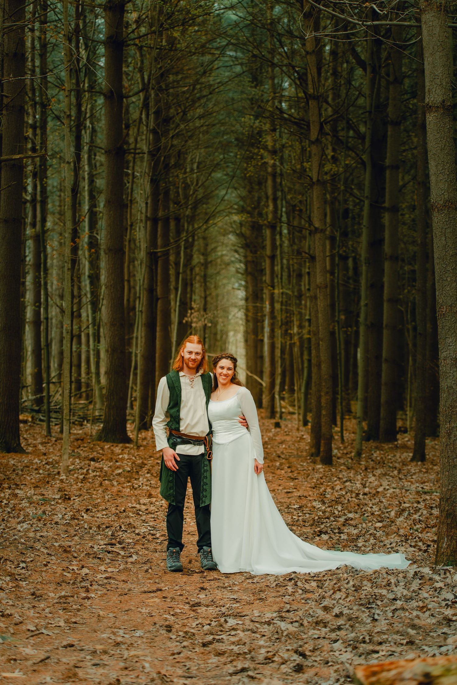 Bride and groom walking hand-in-hand through a pine tree-lined path in the forest.