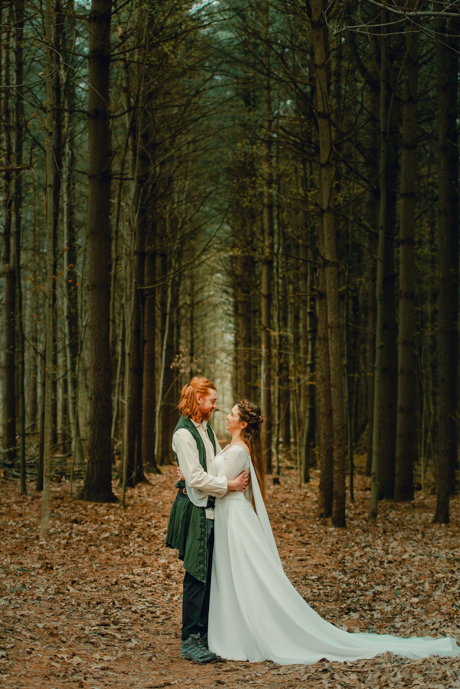 Bride and groom walking hand-in-hand through a pine tree-lined path in the forest.