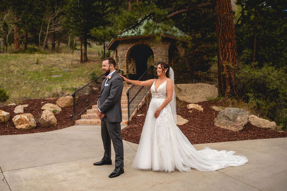 A wedding couple participates in a first look moment outside a rustic stone structure.