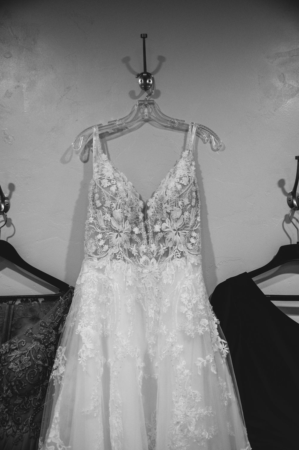 An elegant white wedding dress with intricate lace details and beading hangs on display against a light background.