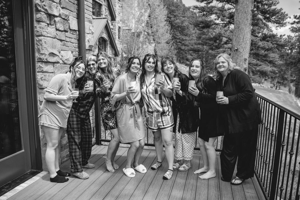A group gathers on a wooden deck outside a stone building for a black and white celebration photo.