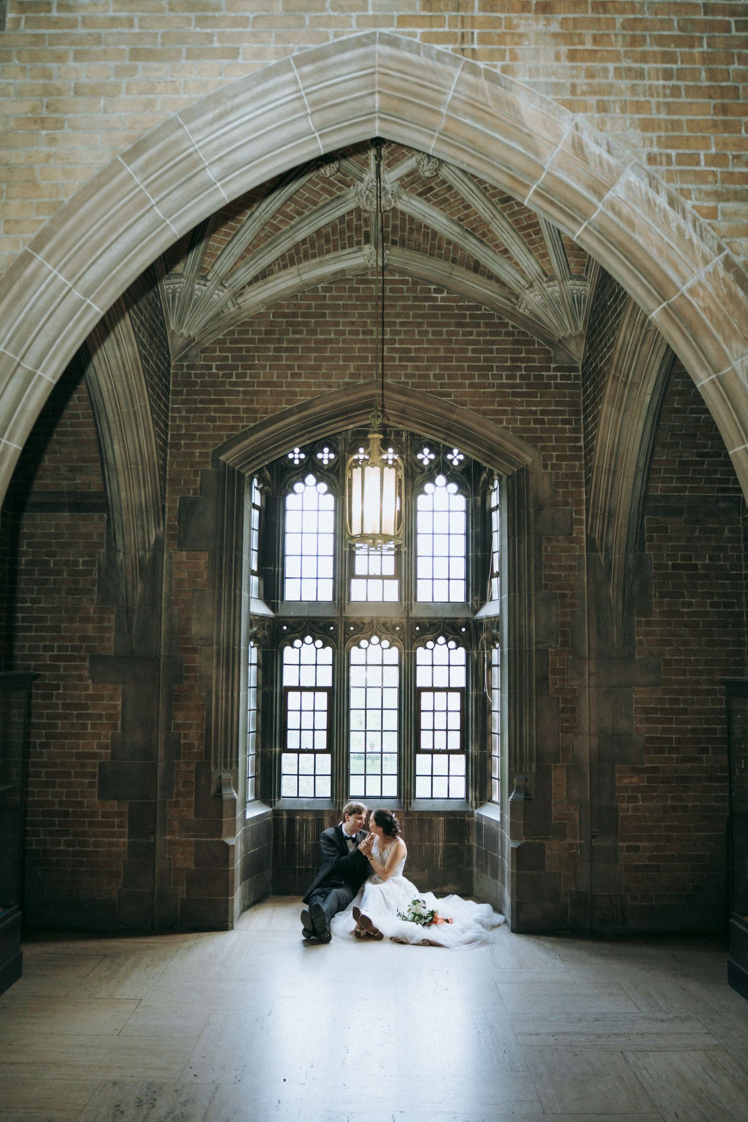 Couple poses in gothic archway with dramatic windows and natural light.