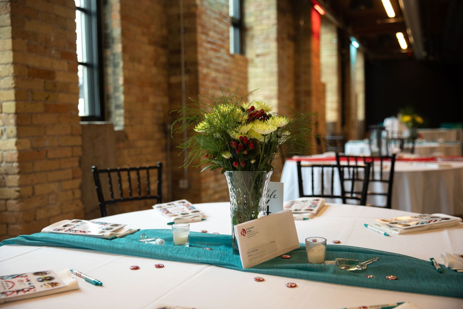 A bingo card and game pieces rest on a round table covered with a white and teal tablecloth.