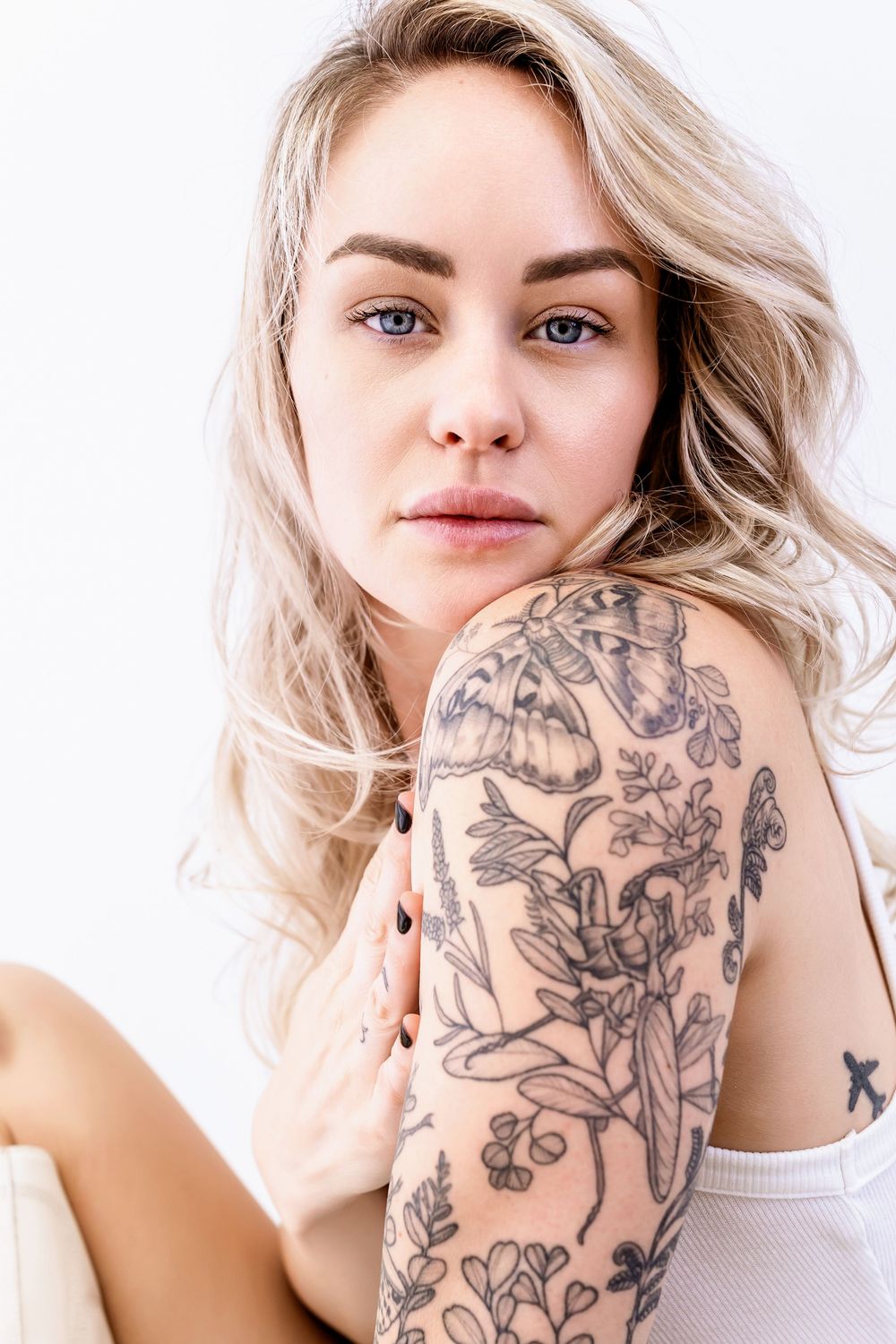 Close up studio portrait showcasing intricate floral arm tattoo sleeve and soft natural lighting.