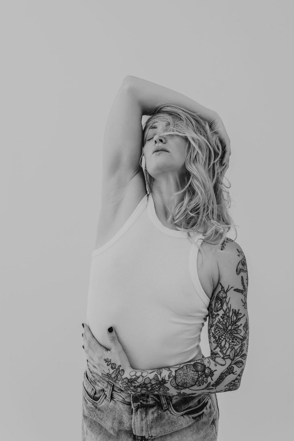Artistic black and white portrait highlighting detailed sleeve tattoos and minimalist white tank top.