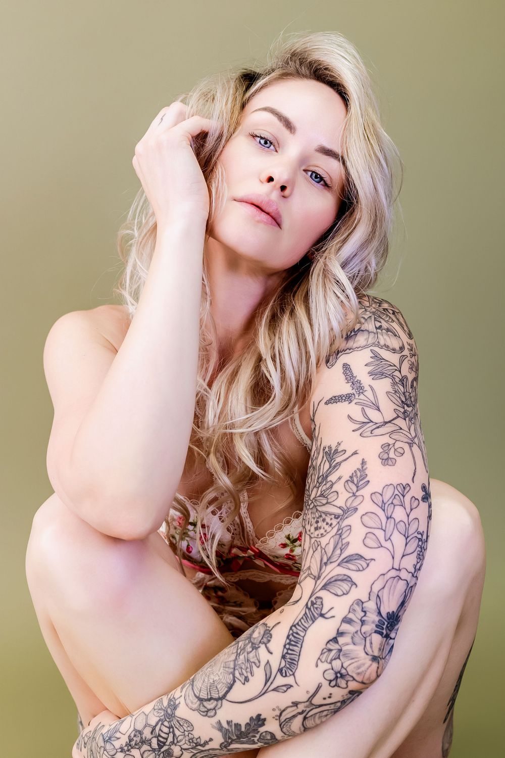 Artistic portrait featuring intricate floral sleeve tattoo against neutral background.