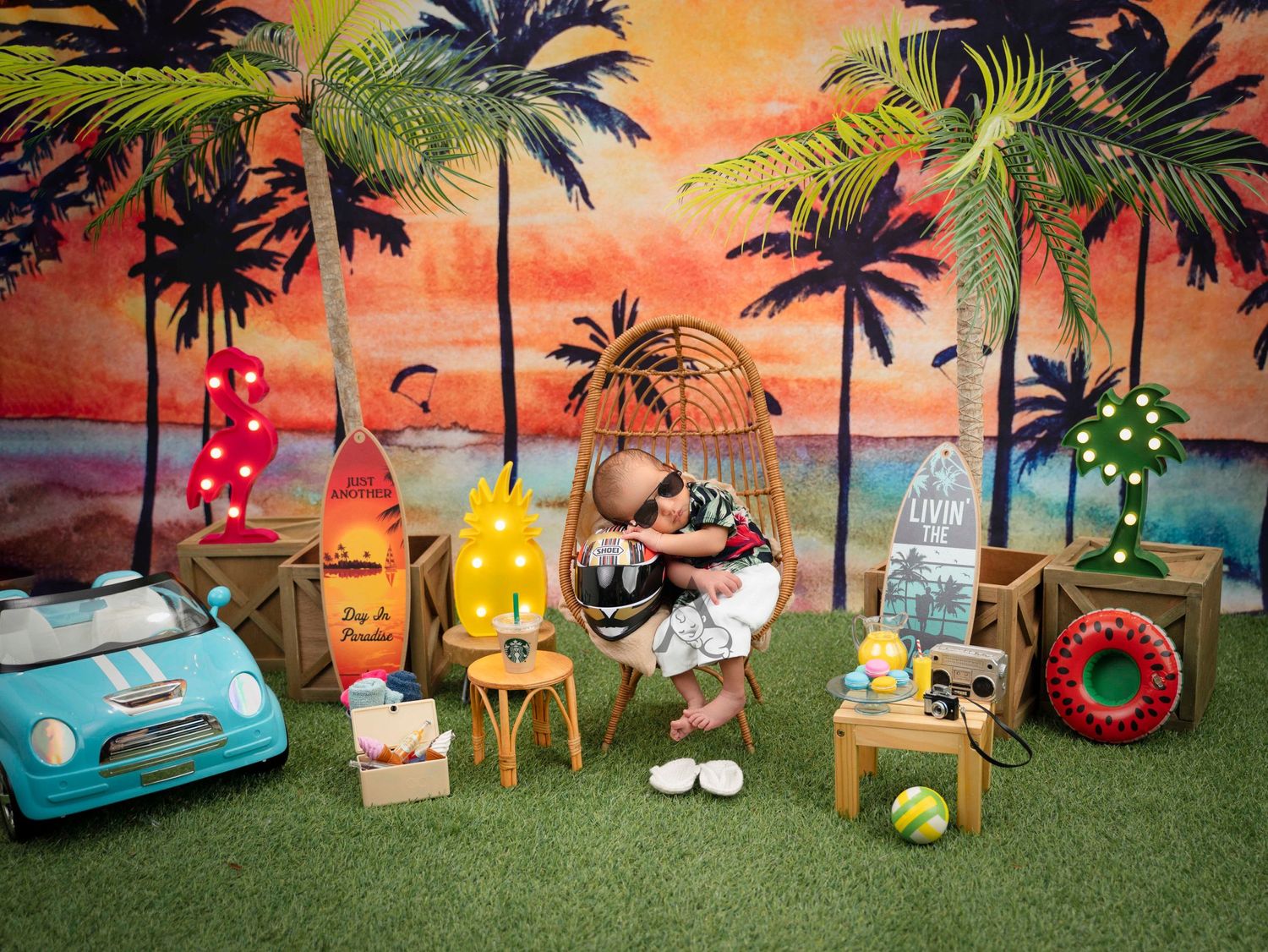Tropical beach themed newborn photo setup with vintage car and rainbow colored lanterns.
