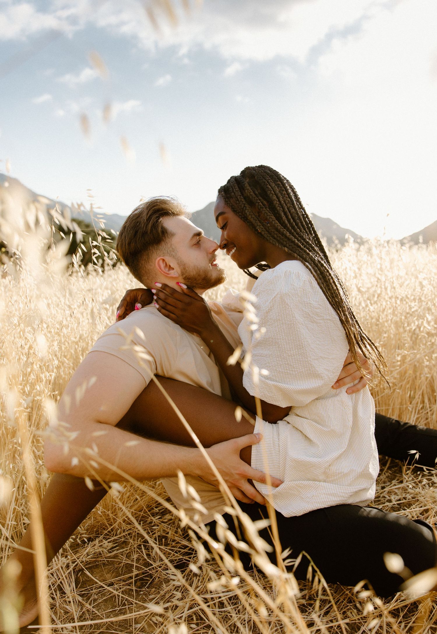 A couple sits intimately in a golden meadow with mountains in the background during sunset.