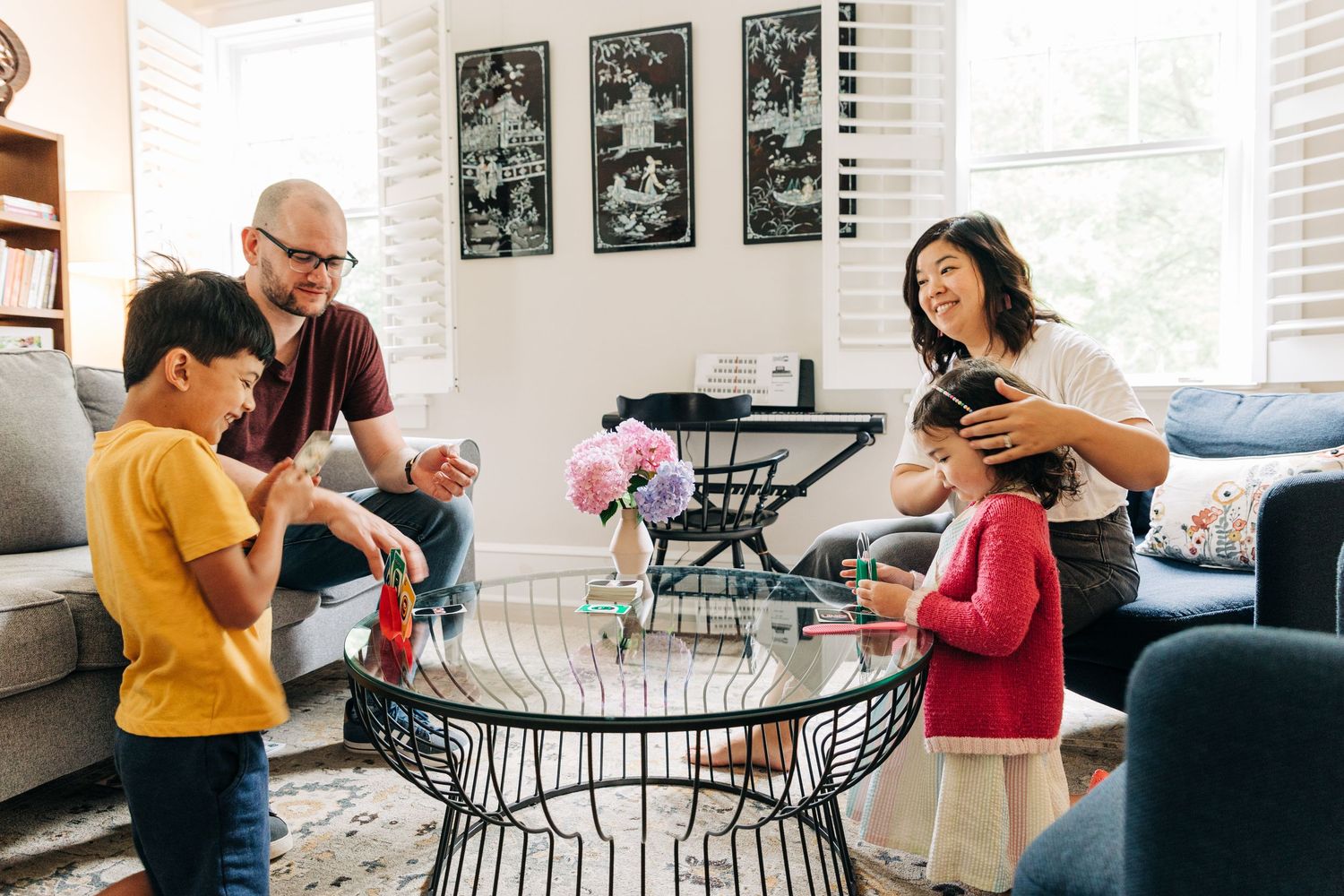 People gathered around a circular metal table with a vase of pink flowers having a relaxed social moment together playing UNO in Charlotte.