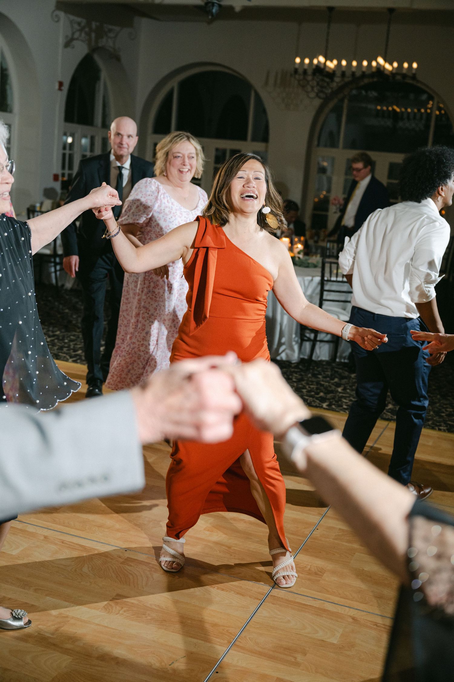 Woman in yellow silk dress laughing joyfully while dancing at an elegant reception venue with patterned carpet.