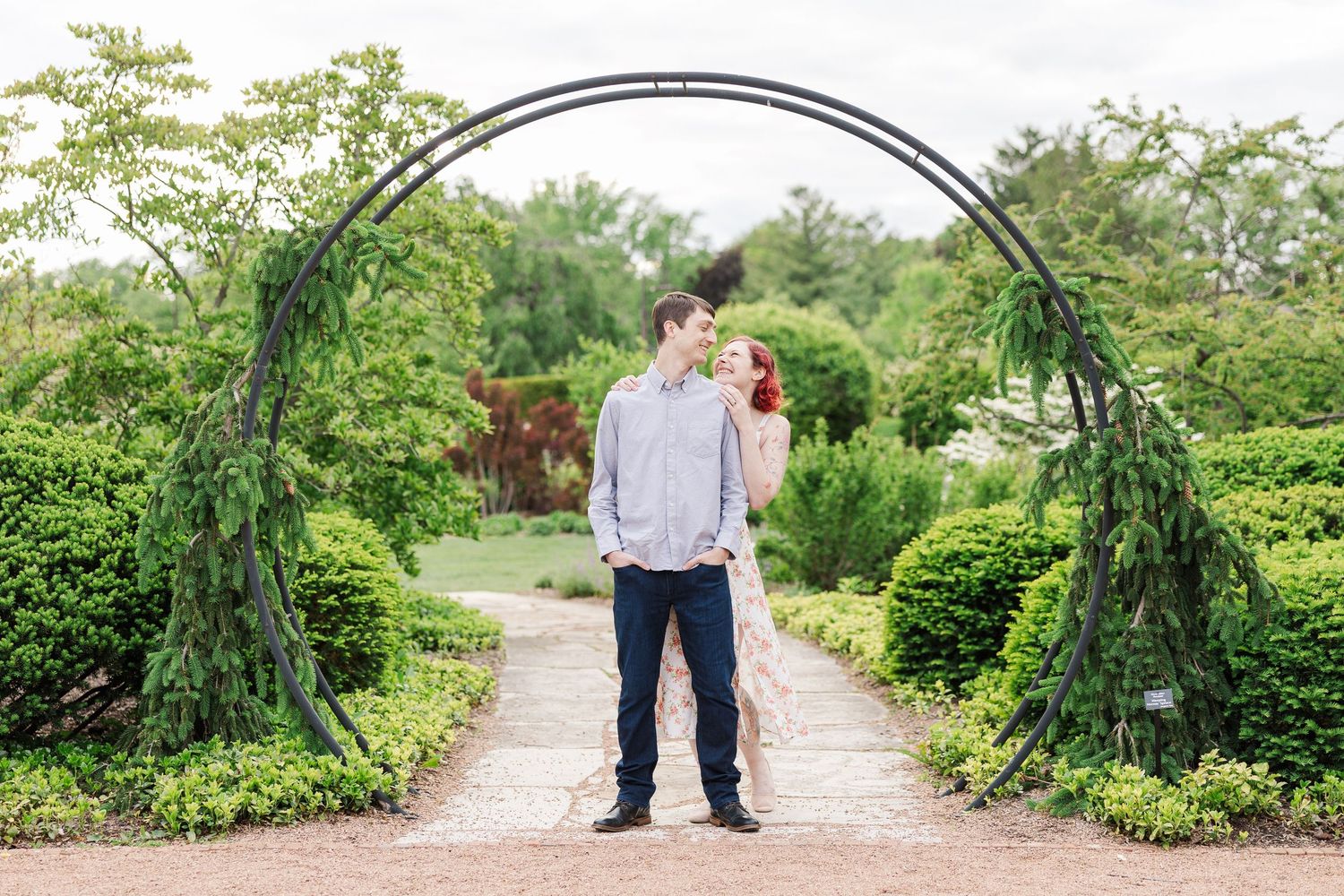 A couple stands together under a garden archway surrounded by lush greenery and a winding path at Cantigny Park