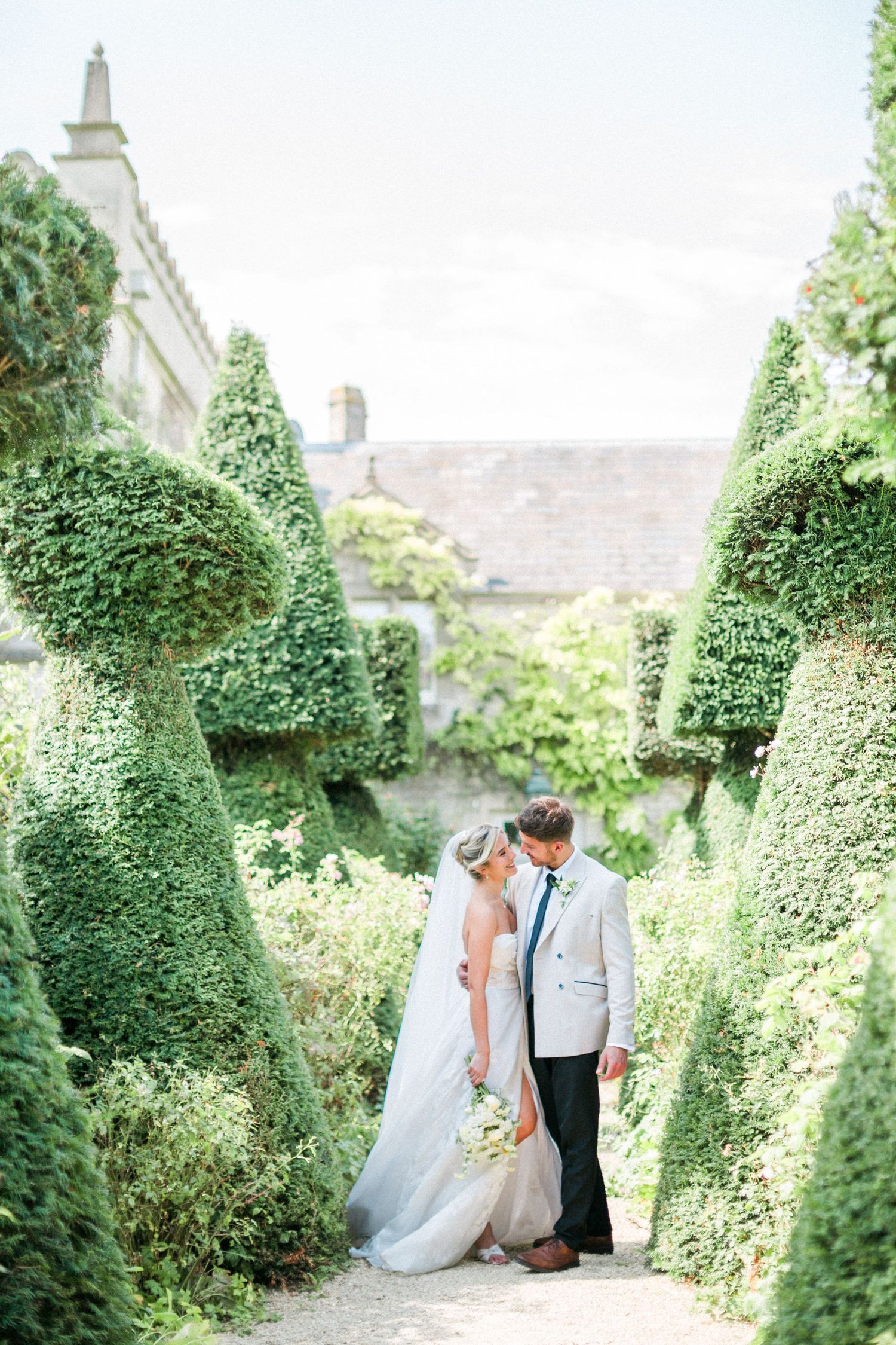 A couple stand on a romantic garden path framed by manicured topiary hedges at Euridge in Wiltshire Hayley Elizabeth Photography