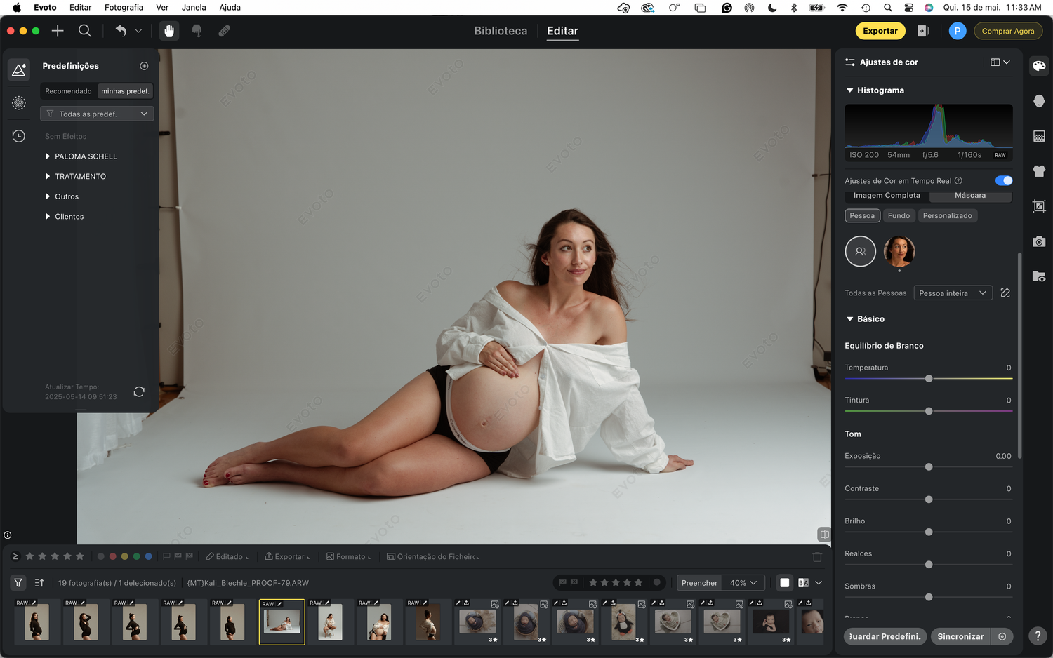 A maternity photo shoot in a studio with a white backdrop shows an artistic pose in soft lighting.