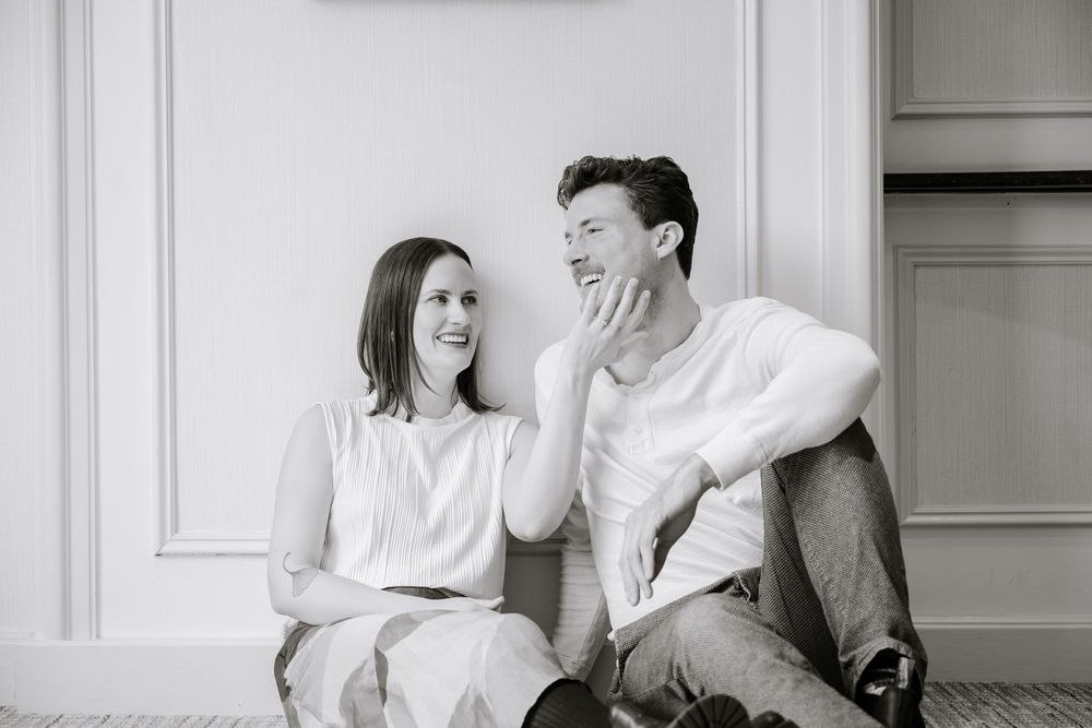 Black and white photo of a couple sitting on floor laughing and sharing a joyful moment together indoors.