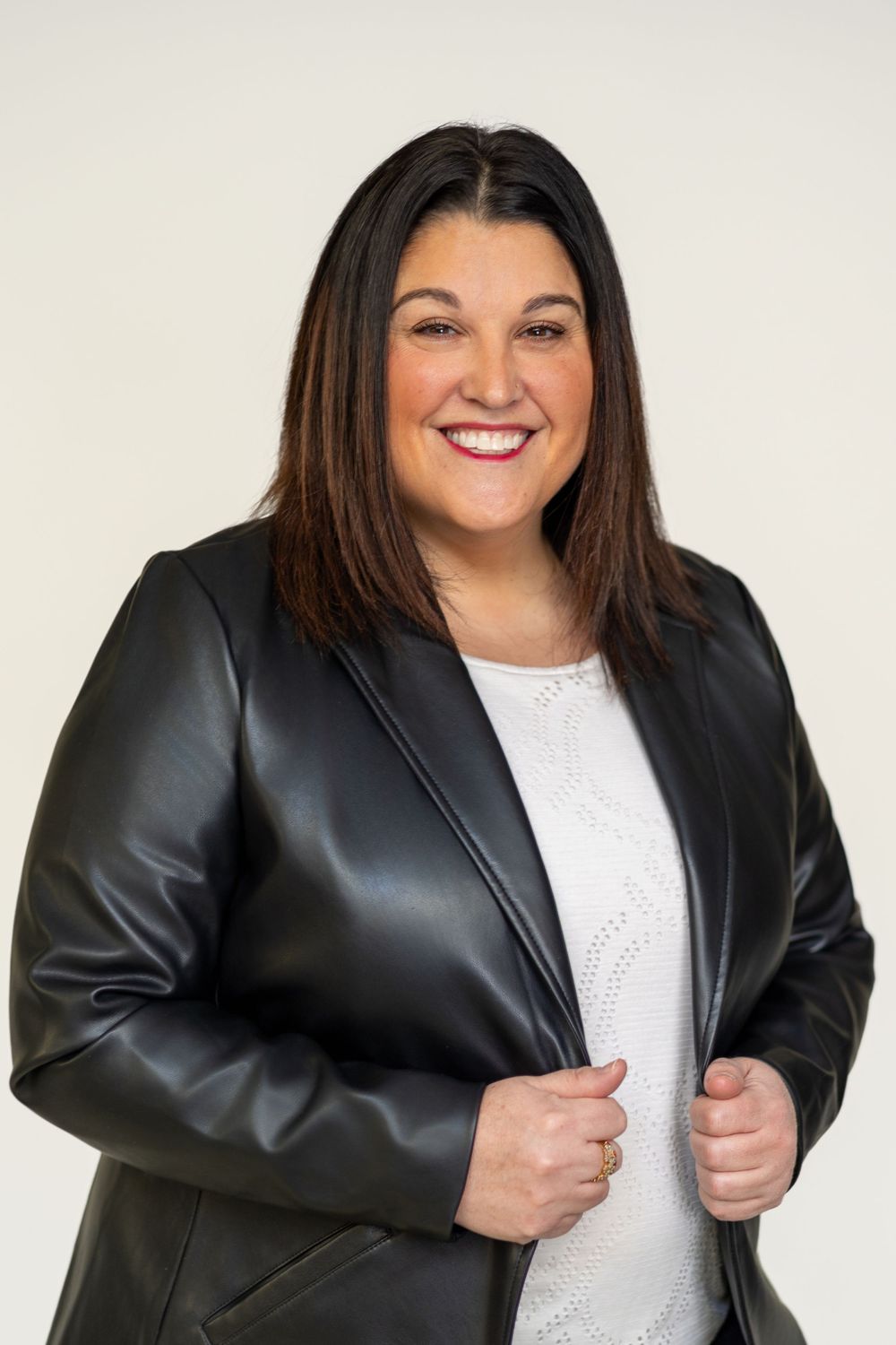 Professional wearing a black leather jacket and white top against white background.