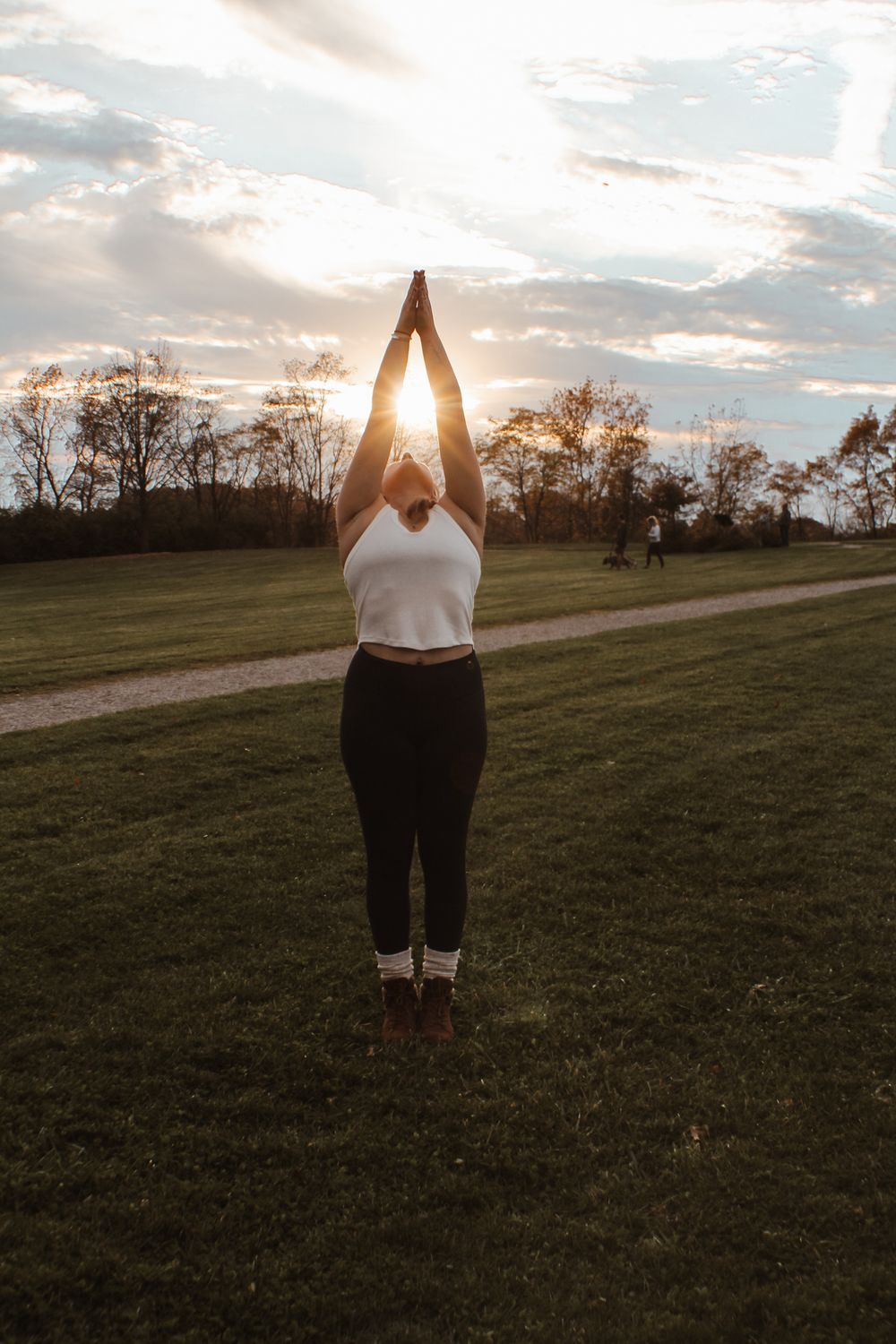 Silhouette against sunset in grassy field with arms raised.